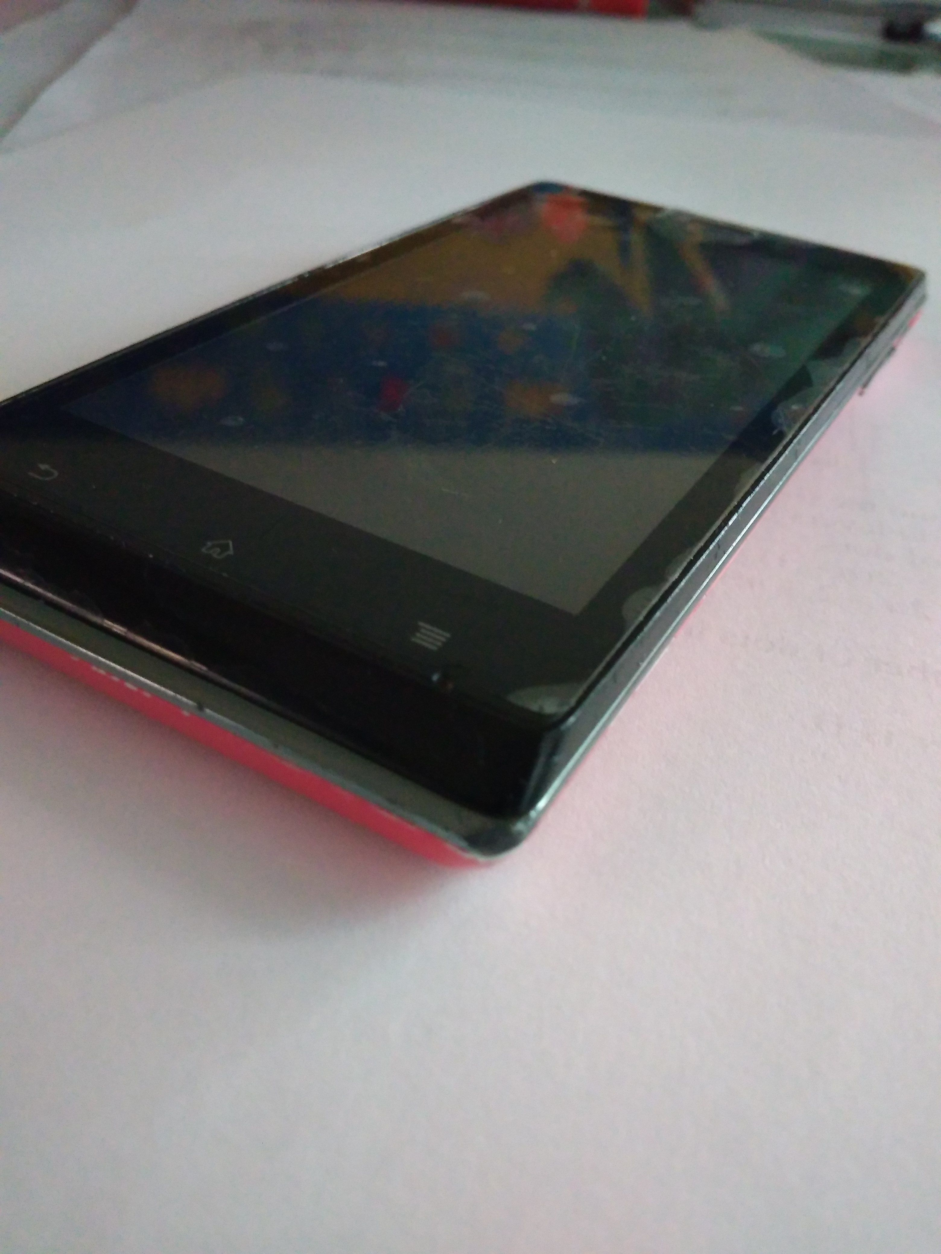 Φωτογραφία ενός κινητού Sony Xperia J σε φούξια χρώμα, σε γωνία τριών τετάρτων πάνω σε ανοιχτό φόντο, με την οθόνη αναμμένη να δείχνει ένα εικαστικό φόντο και τα φωτισμένα soft-keys πλοήγησης από κάτω.